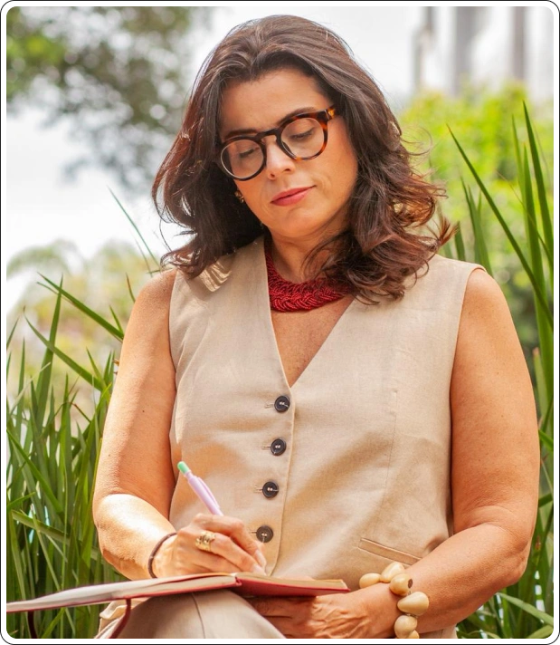 Profa. Dra. Rita Grassi escrevendo em um caderno ao ar livre
