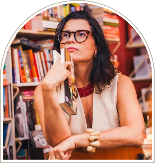 Profa. Dra. Rita Grassi diante de uma estante de livros, com a caneta na mão